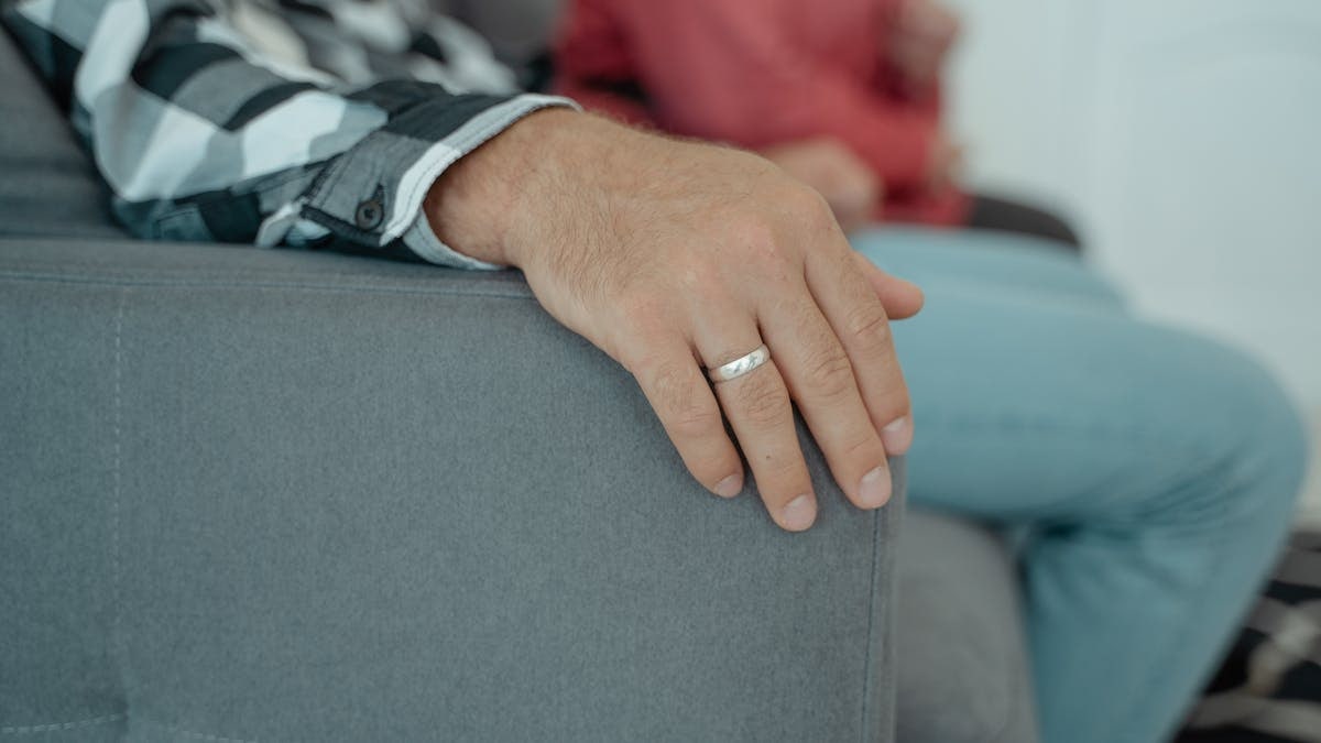 A close-up view of adult hands resting on a couch wearing a wedding ring indoors.